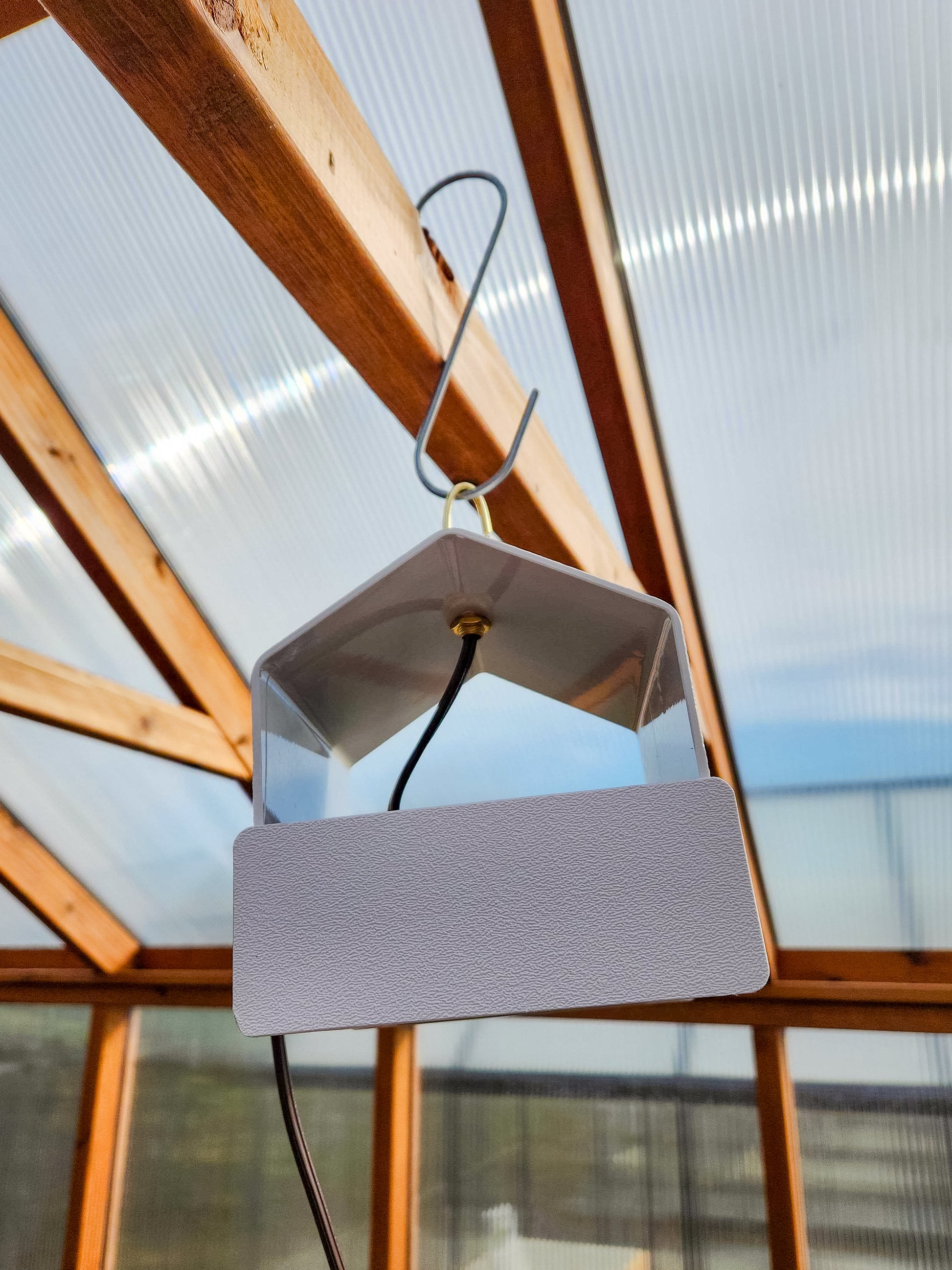 Heat Saver Fan: A side view of the product hanging in a greenhouse